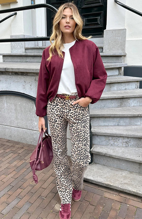 Donna con giacca bordeaux, pantaloni leopardati e borsa abbinata, su gradini di pietra. Moda autunnale, stile urbano chic.