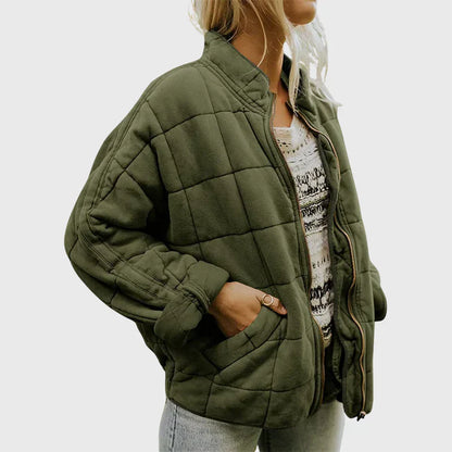 Giacca trapuntata verde oliva da donna, stile casual, con zip frontale e tasche, indossata su maglia bianca a motivi, moda autunnale.