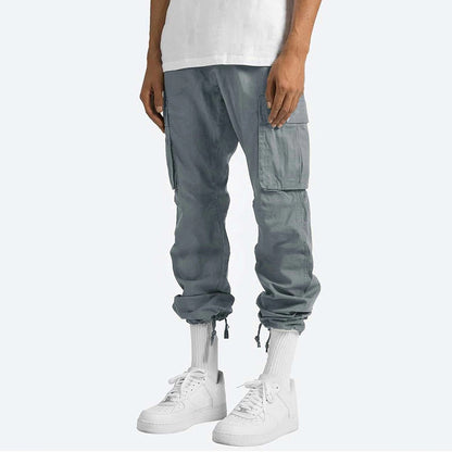 Pantaloni cargo grigi da uomo, tasche laterali, abbinati a scarpe da ginnastica bianche e calzini alti. Stile casual e moderno.