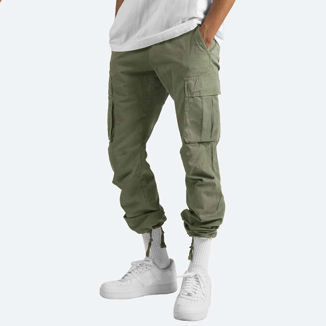 Pantaloni cargo verde oliva da uomo, tasche multiple, stile casual, abbinati a scarpe da ginnastica bianche e calzini alti, moda streetwear.