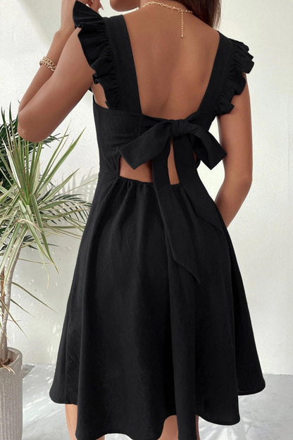 Abito nero estivo con fiocco posteriore, spalline larghe e volant, indossato da donna. Elegante e casual, perfetto per occasioni estive.