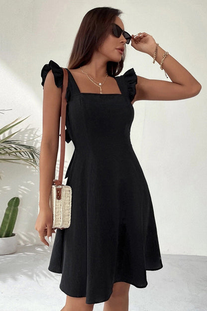 Donna con abito nero estivo, spalline a balze, occhiali da sole, borsa a tracolla in paglia, sfondo bianco minimalista, pianta decorativa.