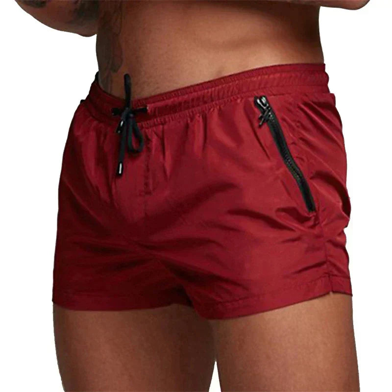 Shorts da bagno uomo rossi con tasche con zip nere, elastico in vita e laccetti. Design moderno, ideale per nuoto e spiaggia.
