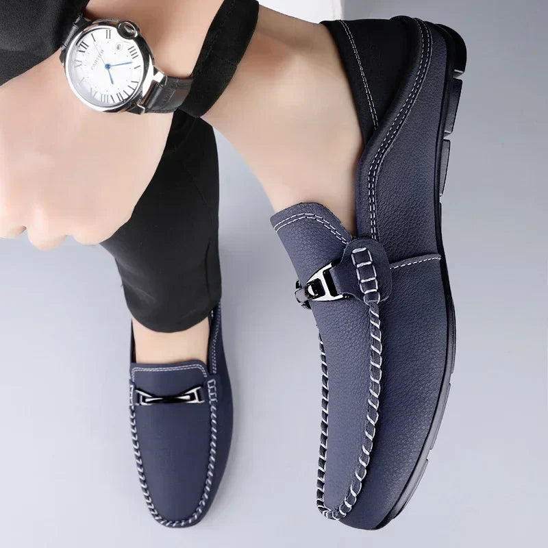 Scarpe mocassino uomo blu scuro eleganti, cuciture bianche a contrasto, fibbia metallica, indossate con pantaloni neri. Orologio da polso argento.