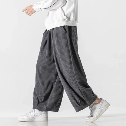 Pantaloni larghi grigi a righe, indossati con felpa bianca e sneakers bianche, moda casual uomo, stile streetwear moderno.
