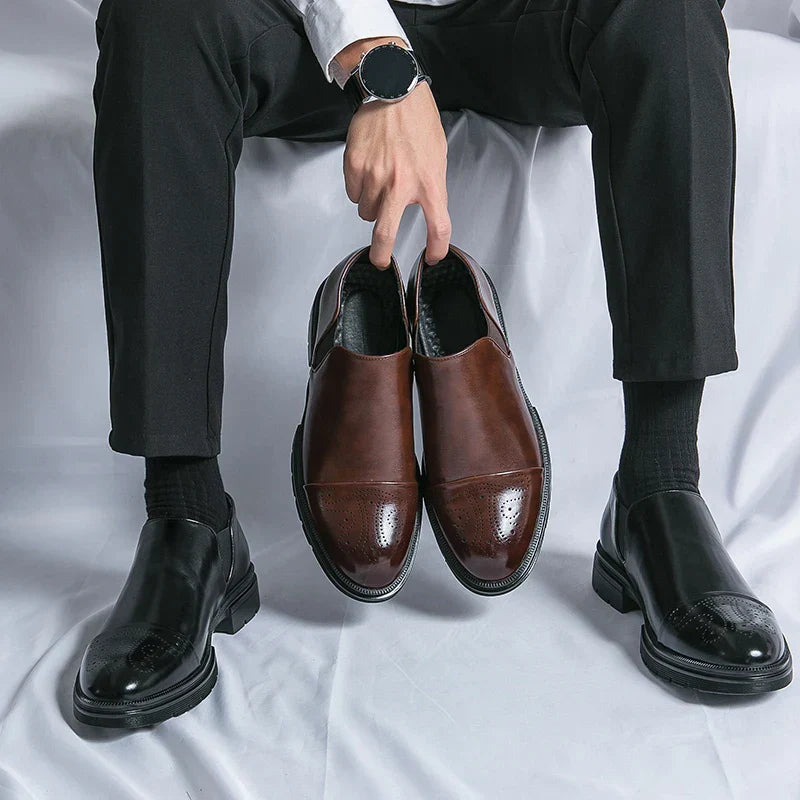 Uomo seduto con pantaloni neri e orologio, tiene scarpe eleganti marroni. Scarpe nere indossate. Moda maschile, calzature formali.