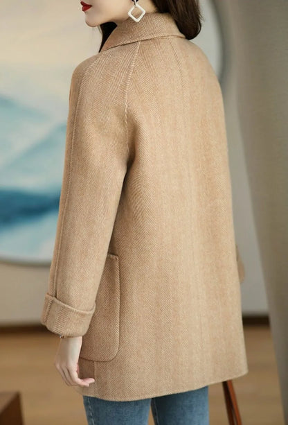 Donna con cappotto beige elegante, tessuto a spina di pesce, indossa jeans blu. Moda autunnale, stile casual chic, dettagli sartoriali.