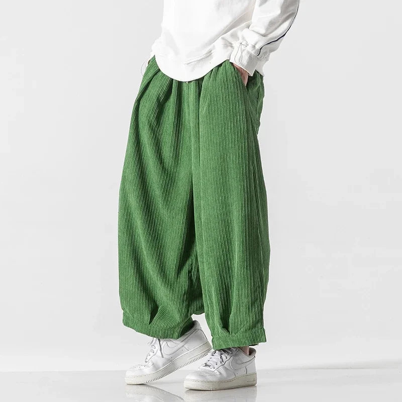 Pantaloni larghi verdi in tessuto a coste, indossati con sneakers bianche e maglia bianca. Moda casual, stile urbano, abbigliamento comodo.