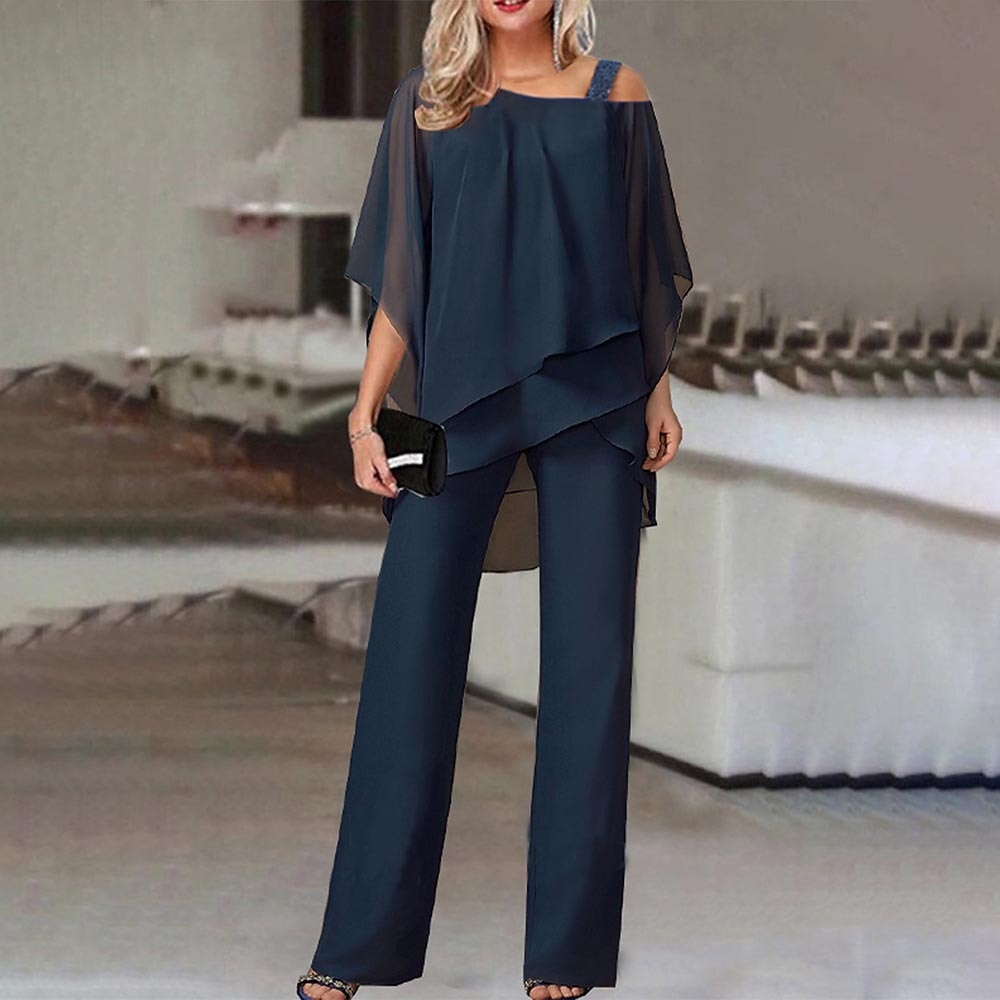 Donna in elegante tuta blu scuro con top asimmetrico e pantaloni larghi, accessoriata con pochette nera. Moda femminile, abbigliamento da sera.