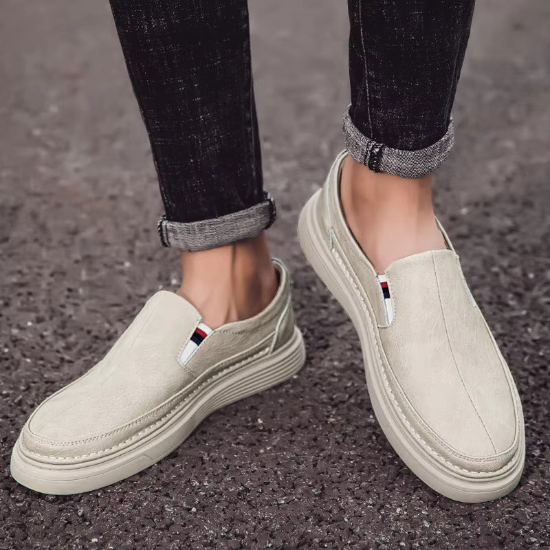 Scarpe slip-on beige da uomo su strada asfaltata, jeans scuri arrotolati. Calzature casual eleganti, comode e alla moda per ogni occasione.
