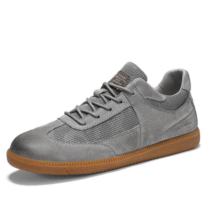 Scarpa sportiva grigia in pelle scamosciata con suola in gomma marrone, design traspirante a rete, ideale per moda casual e comfort quotidiano.