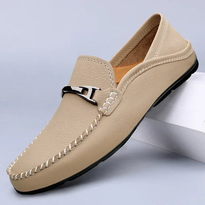Mocassino beige da uomo in pelle, con cuciture bianche e dettaglio metallico, su sfondo grigio. Scarpe eleganti, moda maschile, calzature di lusso.