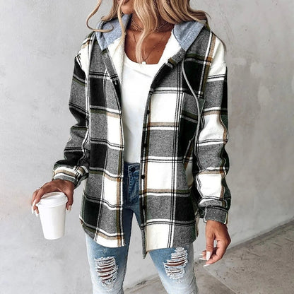 Donna con camicia a quadri bianca e nera, cappuccio grigio, jeans strappati e maglietta bianca, tiene una tazza di caffè. Moda casual autunnale.