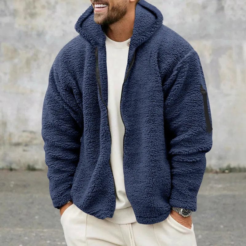 Uomo con giacca in pile blu, cappuccio, tasca sulla manica, sfondo grigio. Moda invernale, abbigliamento casual, stile moderno.