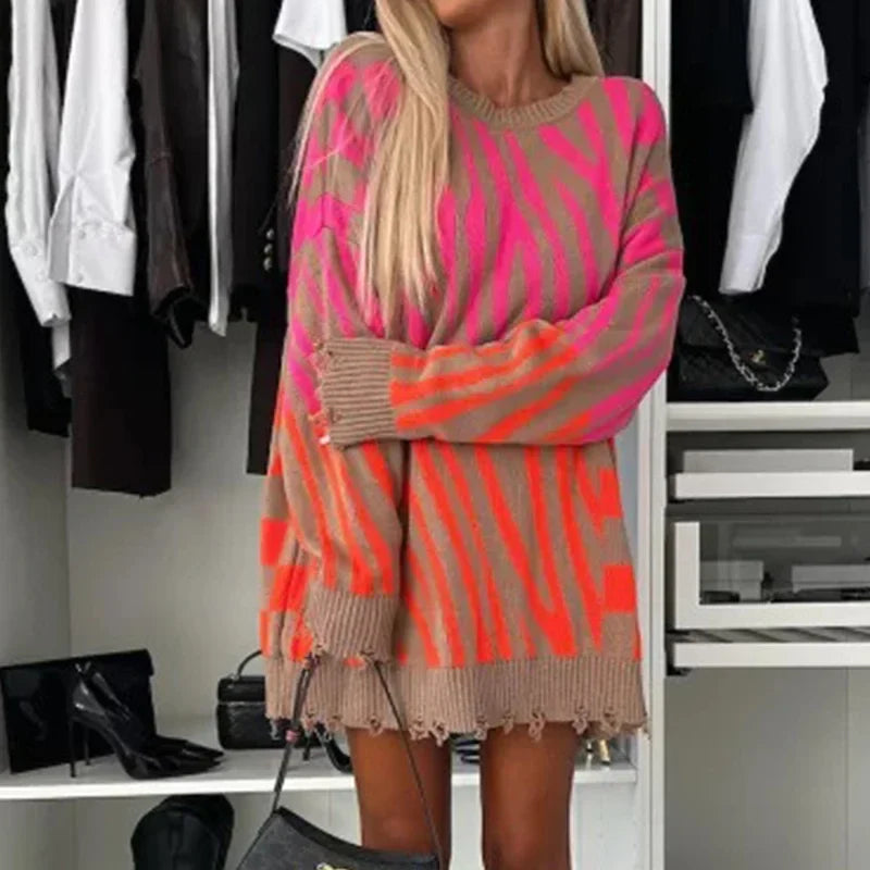 Donna con maglione oversize a righe rosa e arancioni, in piedi davanti a un armadio aperto con abiti e scarpe. Moda autunnale, look casual chic.
