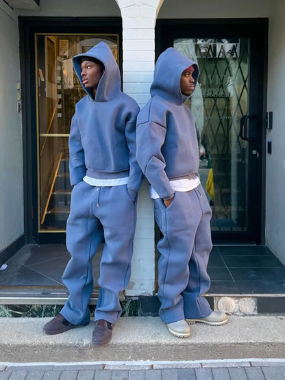 Due ragazzi in tuta sportiva blu con cappuccio, appoggiati a un muro. Moda urbana, abbigliamento casual, streetwear contemporaneo.