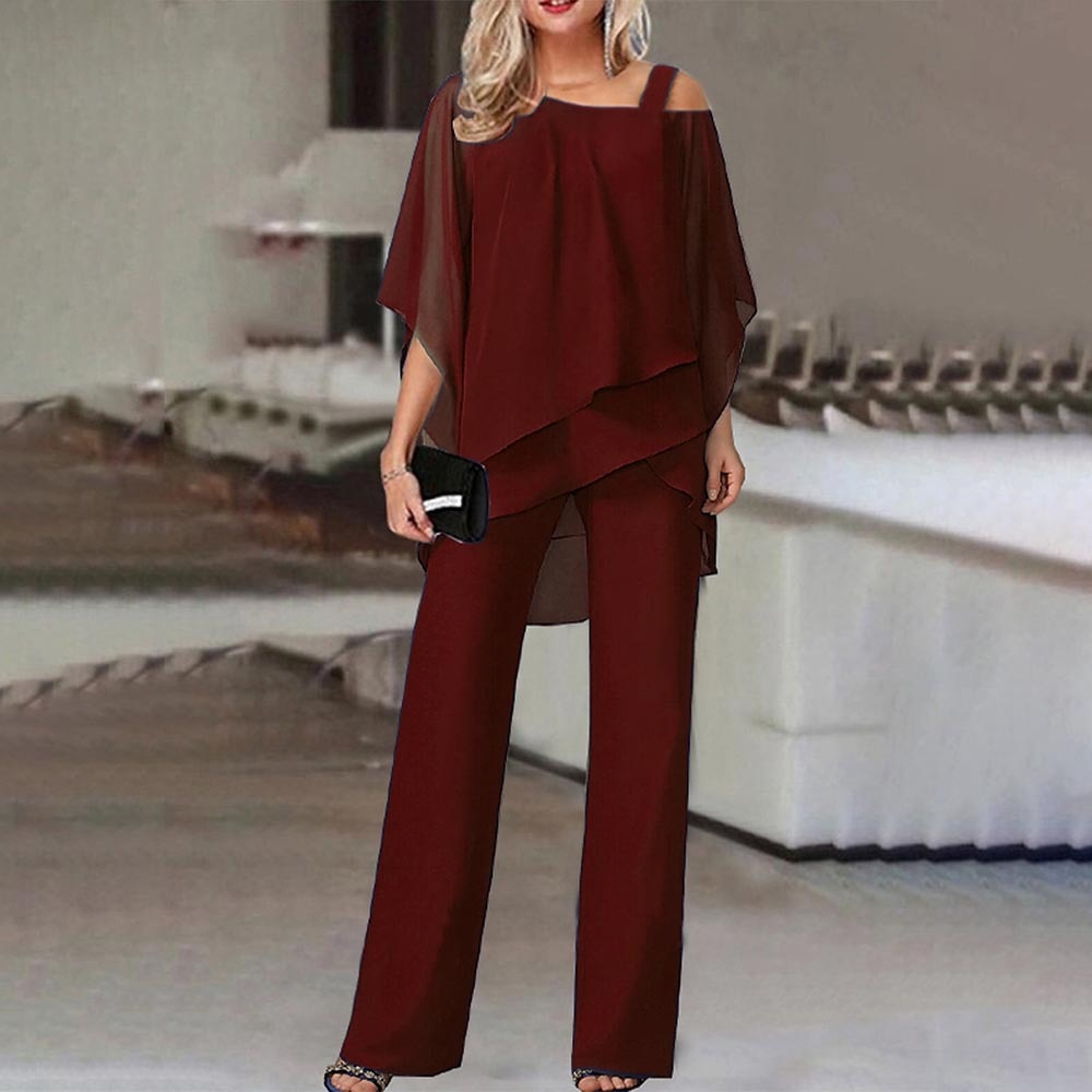Donna in elegante completo rosso bordeaux, composto da tunica asimmetrica e pantaloni larghi, con pochette nera. Moda femminile, abbigliamento elegante.