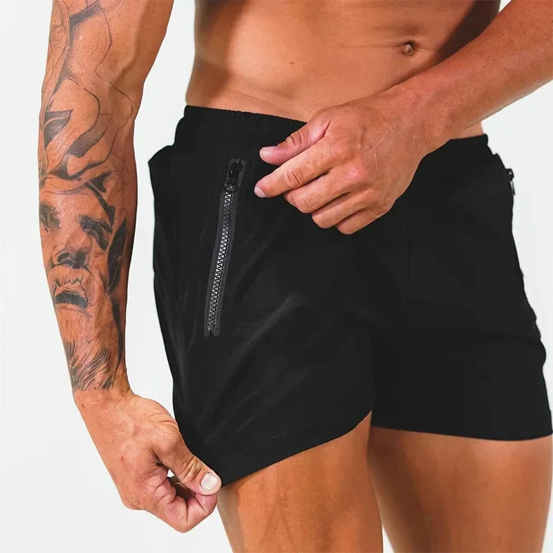 Uomo muscoloso con tatuaggio indossa pantaloncini sportivi neri con tasca con zip. Fitness, abbigliamento sportivo, moda uomo.