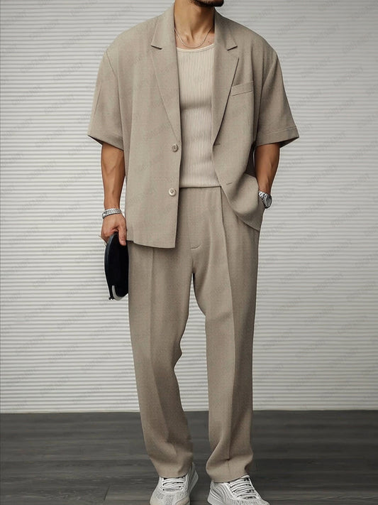 Uomo in completo beige estivo, giacca e pantaloni larghi, maglia a coste, scarpe bianche, orologio argento, moda maschile elegante e casual.