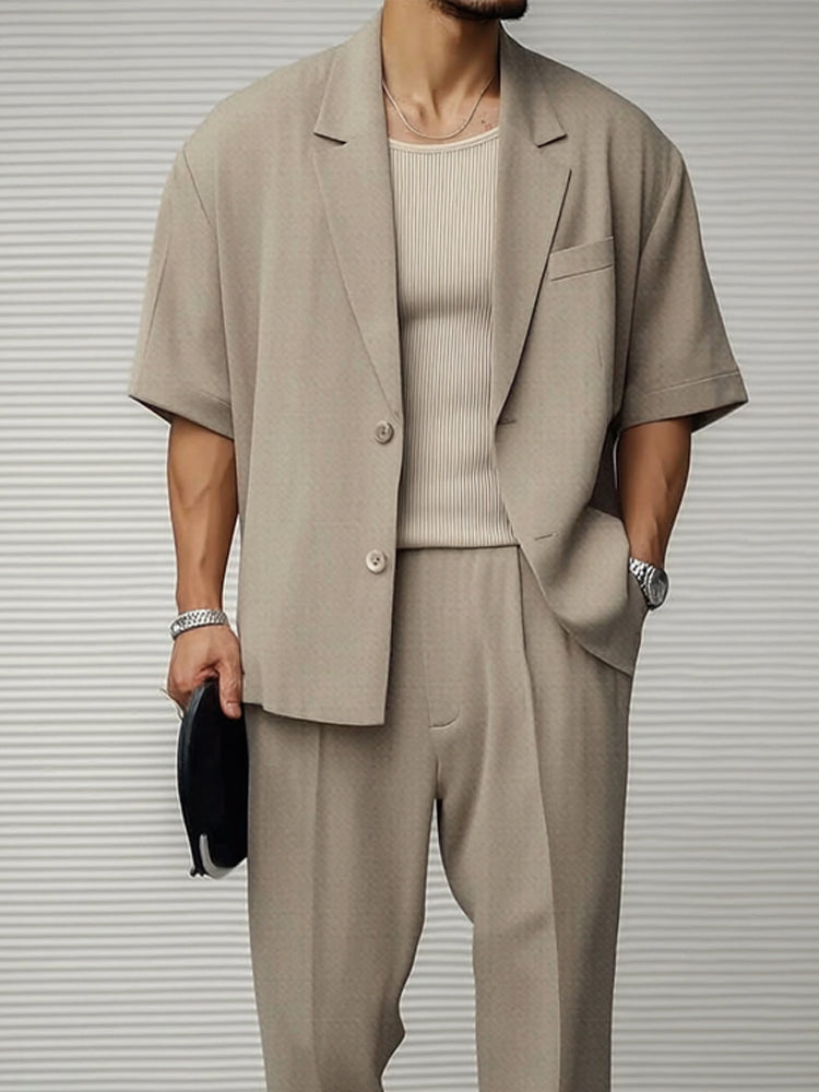 Uomo in abito beige estivo, giacca a maniche corte, pantaloni coordinati, maglia a coste, orologio argento, moda maschile elegante e casual.