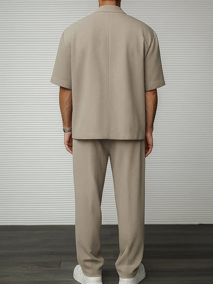 Uomo in completo beige minimalista, giacca e pantaloni coordinati, su sfondo a righe. Moda maschile elegante, stile casual chic.