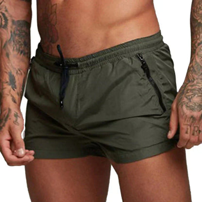 Uomo con pantaloncini da bagno verdi, tatuaggi sulle braccia, cerniere laterali, stile sportivo. Moda estiva, abbigliamento mare maschile.