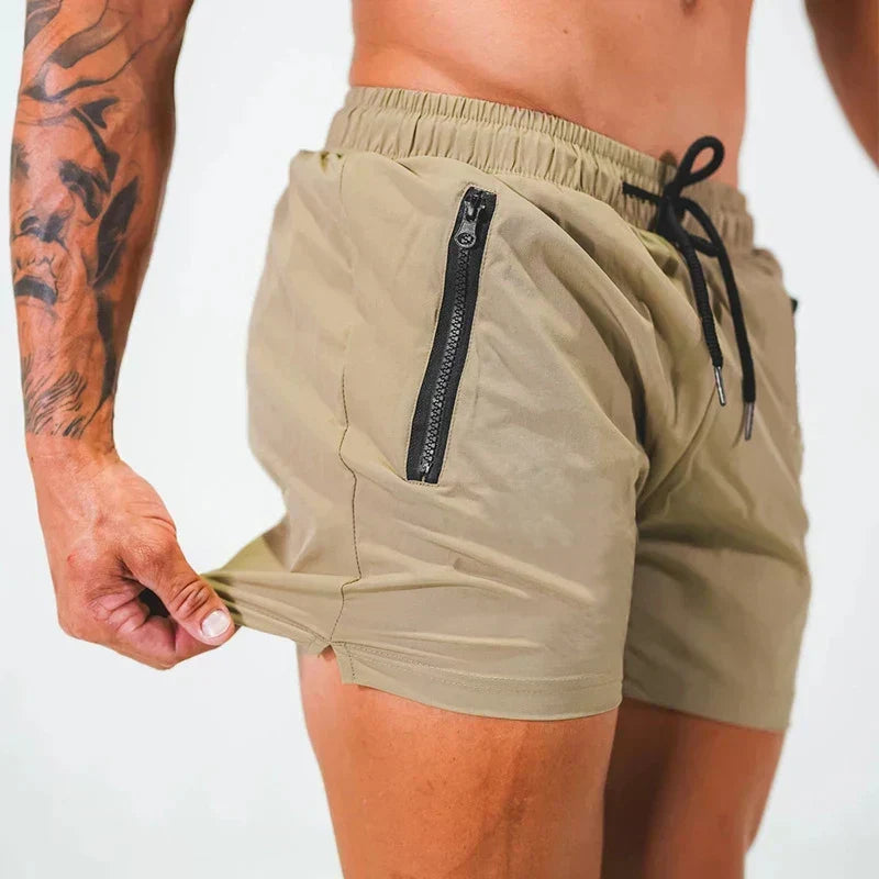 Shorts sportivi beige con tasche con zip, indossati da uomo muscoloso con tatuaggi. Abbigliamento fitness estivo, moda uomo casual.