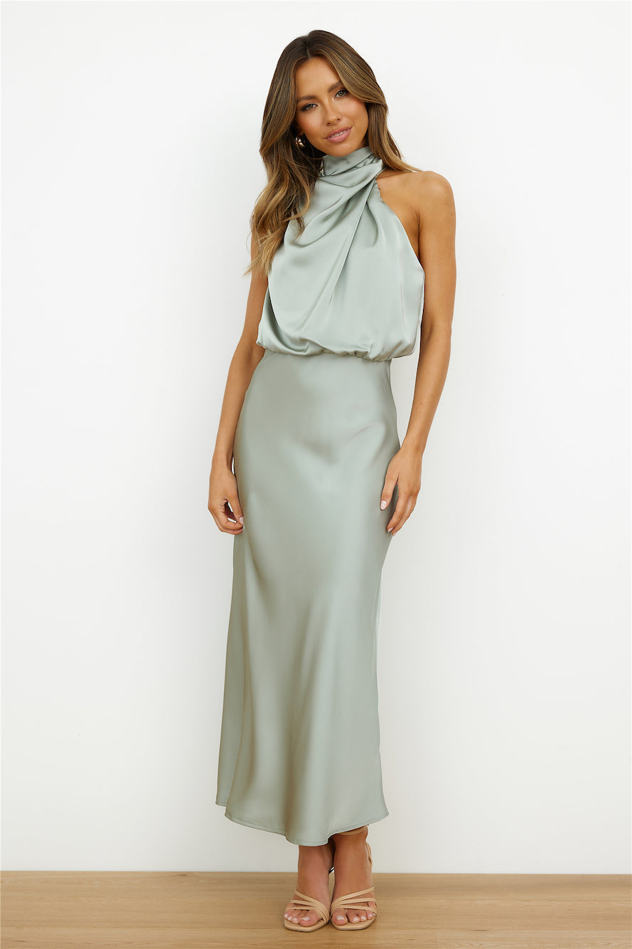 Donna in abito lungo di seta verde salvia, senza maniche, con scollo drappeggiato. Elegante moda femminile, abbigliamento da sera sofisticato.