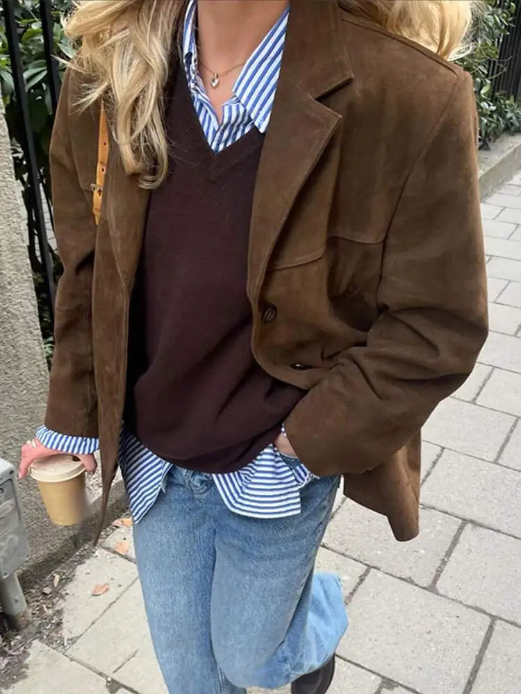 Donna con giacca marrone in pelle scamosciata, camicia a righe blu, maglione marrone, jeans e caffè da asporto. Moda autunnale casual chic.
