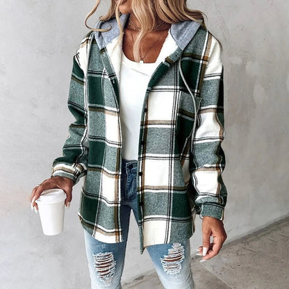 Donna con camicia a quadri verde e bianca, cappuccio grigio, jeans strappati, tiene bicchiere di caffè. Moda casual autunnale.