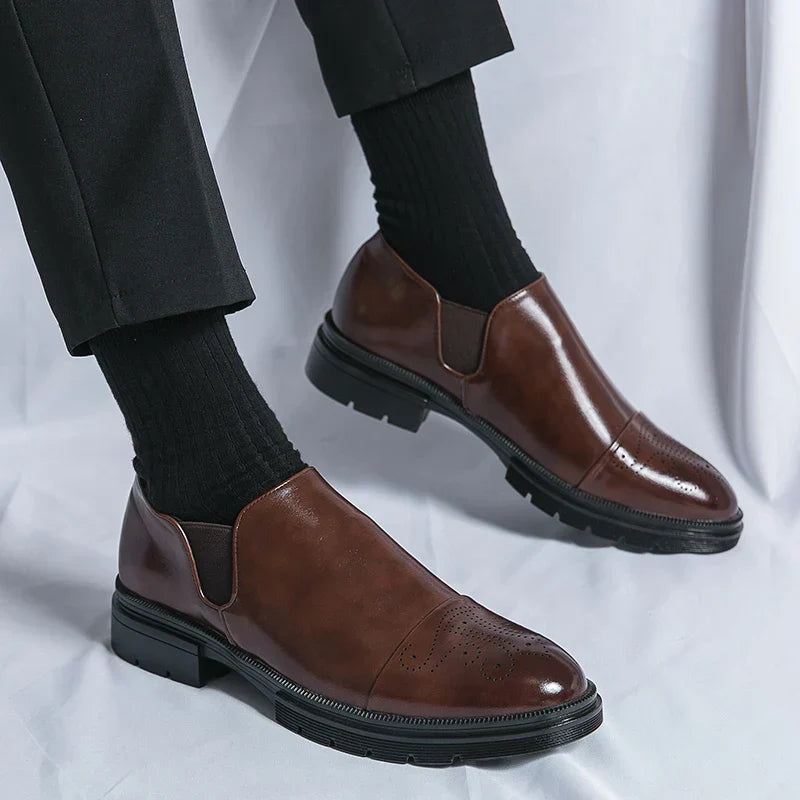 Scarpe eleganti da uomo in pelle marrone, design slip-on, suola robusta, indossate con calzini neri e pantaloni scuri. Moda maschile formale.