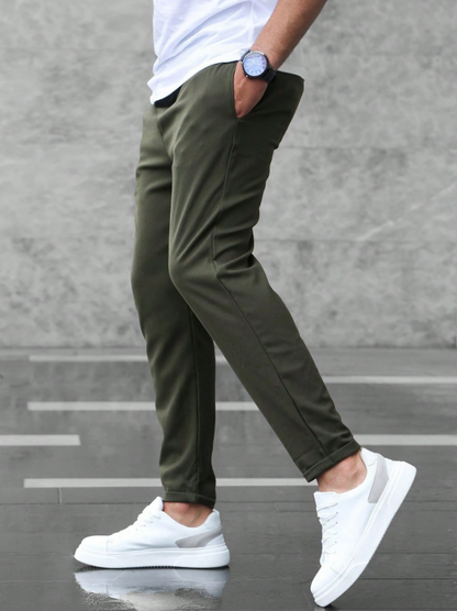 Uomo con pantaloni verde oliva, scarpe da ginnastica bianche e orologio blu, cammina su pavimento grigio. Moda casual maschile, stile urbano.