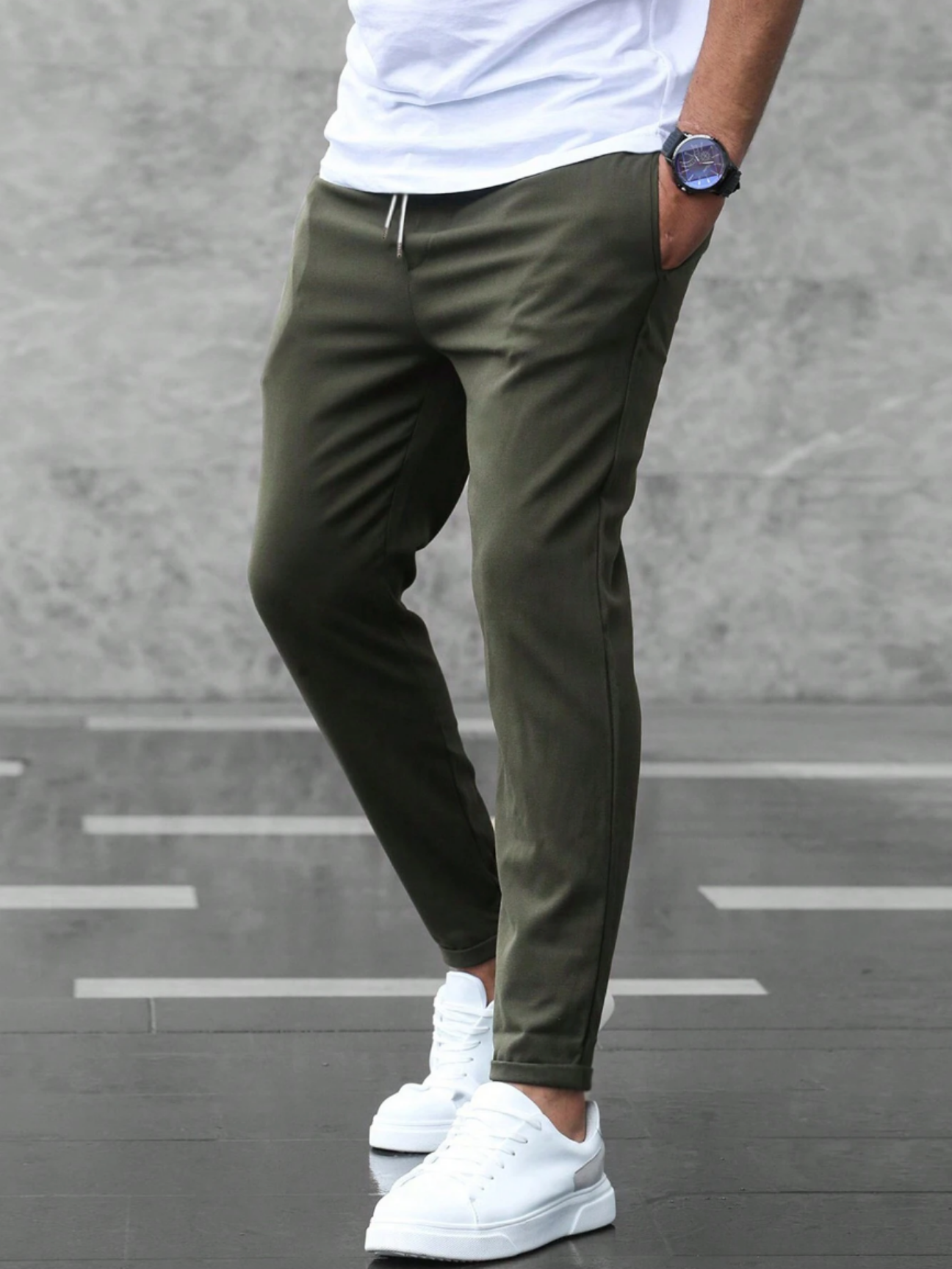 Pantaloni jogger verde oliva da uomo, abbinati a scarpe da ginnastica bianche e maglietta bianca, moda casual urbana, sfondo grigio.