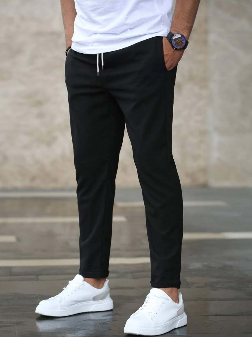 Uomo con pantaloni neri casual e scarpe da ginnastica bianche, moda maschile urbana, abbigliamento comodo, stile moderno, sfondo neutro.