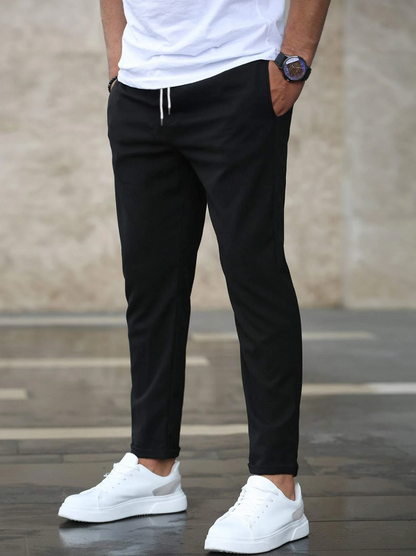 Uomo con pantaloni neri casual e scarpe da ginnastica bianche, moda maschile urbana, abbigliamento comodo, stile moderno, sfondo neutro.