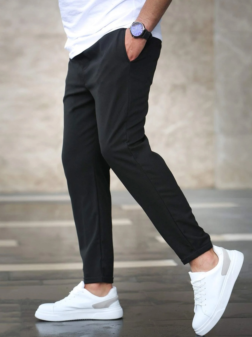 Uomo con pantaloni neri eleganti e scarpe da ginnastica bianche, cammina su marciapiede. Moda maschile casual, orologio da polso blu.