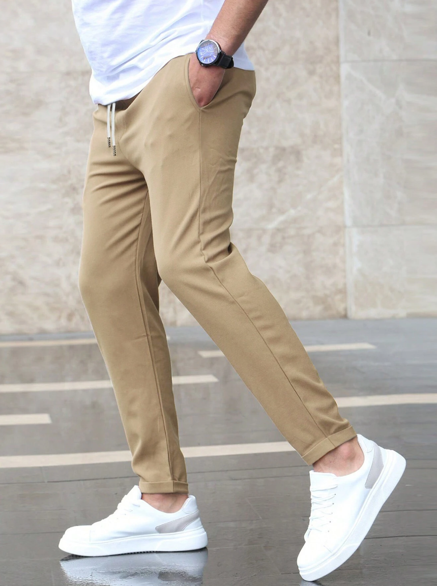 Pantaloni chino beige da uomo, abbinati a scarpe da ginnastica bianche e maglietta bianca, moda casual maschile, stile urbano moderno.