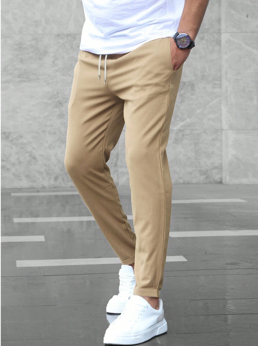 Pantaloni chino beige da uomo, abbinati a scarpe da ginnastica bianche e maglietta bianca. Stile casual moderno, moda maschile urbana.