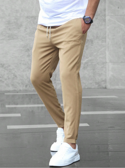 Pantaloni chino beige da uomo, abbinati a scarpe da ginnastica bianche e maglietta bianca, moda casual maschile, sfondo grigio urbano.
