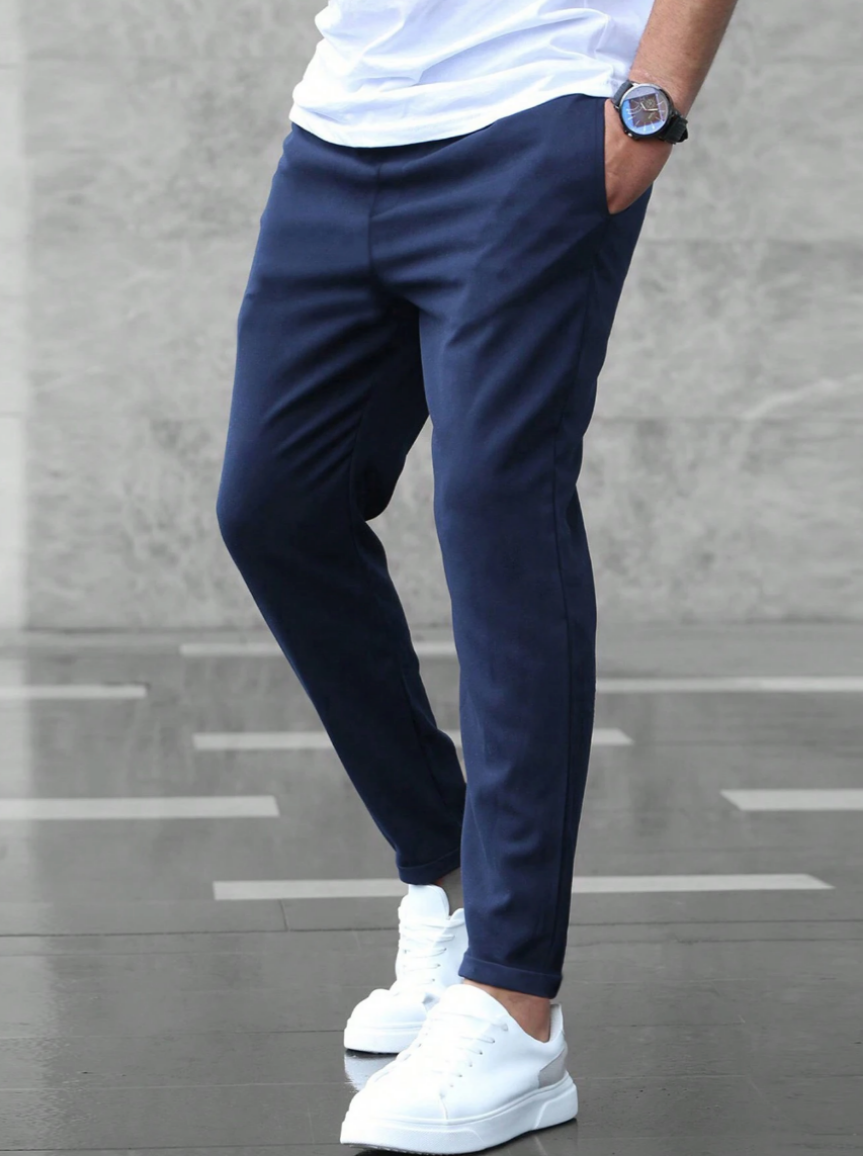 Pantaloni eleganti blu da uomo, abbinati a scarpe da ginnastica bianche, su sfondo grigio. Moda maschile casual chic.