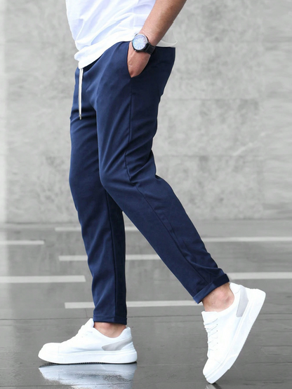 Uomo con pantaloni jogger blu navy, maglietta bianca e scarpe da ginnastica bianche, cammina su pavimento grigio. Moda casual maschile.