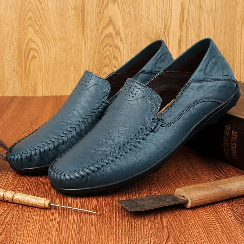Scarpe mocassini in pelle blu da uomo su sfondo in legno, strumenti artigianali accanto. Eleganti, casual, perfette per moda maschile.