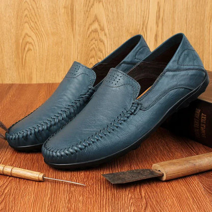 Scarpe mocassini in pelle blu da uomo su sfondo in legno, strumenti artigianali accanto. Eleganti, casual, perfette per moda maschile.
