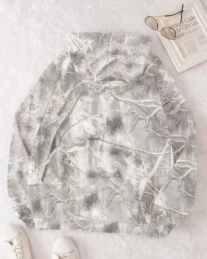 Felpa con cappuccio mimetica grigia, motivo foresta invernale, su sfondo bianco. Include occhiali da sole, rivista e scarpe bianche.