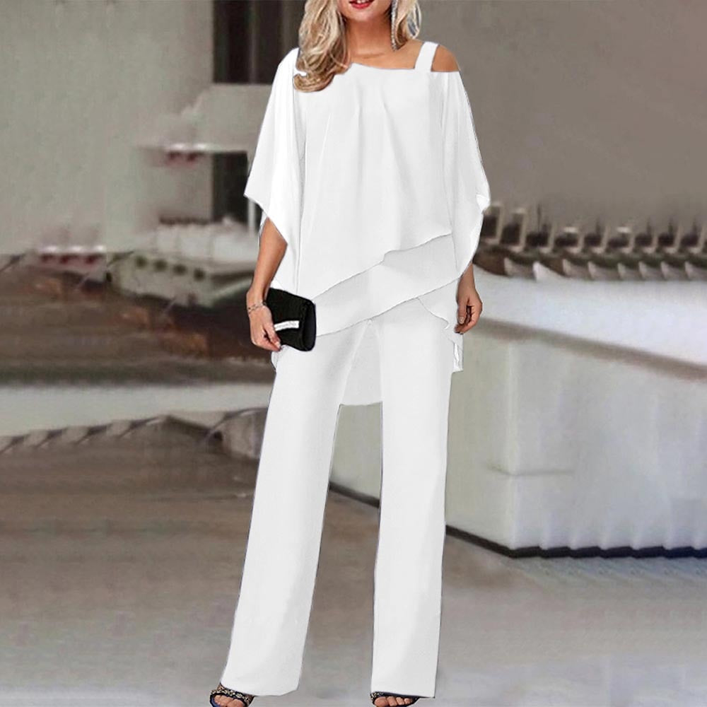 Donna in elegante completo bianco, blusa asimmetrica e pantaloni larghi, con borsa nera. Moda femminile, abbigliamento estivo chic.
