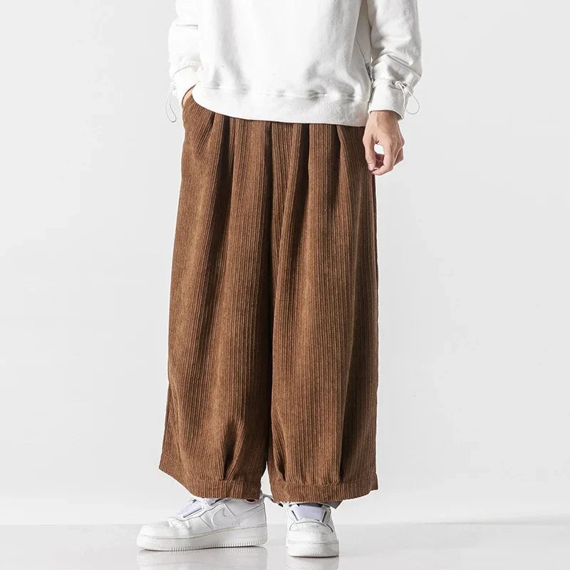 Pantaloni larghi in velluto a coste marroni, indossati con felpa bianca e scarpe da ginnastica bianche. Moda casual uomo, stile autunnale.