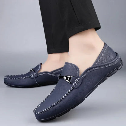 Scarpe mocassini uomo in pelle blu scuro, cuciture bianche, suola antiscivolo, indossate con pantaloni neri. Eleganti e comode per ogni occasione.