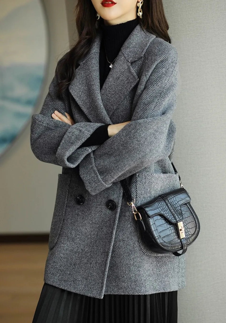 Donna con cappotto grigio elegante, borsa a tracolla nera in pelle, abbigliamento autunnale chic, moda femminile moderna, sfondo interno neutro.