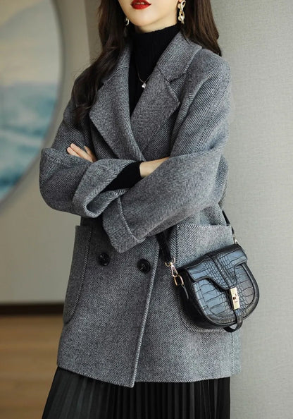 Donna con cappotto grigio elegante, borsa a tracolla nera in pelle, abbigliamento autunnale chic, moda femminile moderna, sfondo interno neutro.