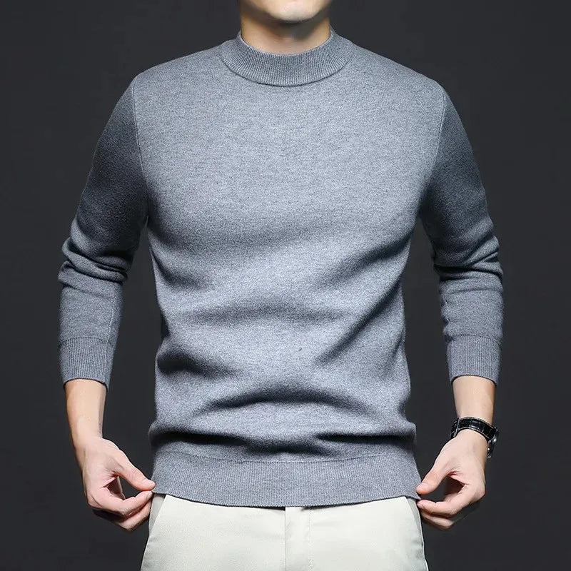 Maglione grigio uomo, maniche lunghe, collo alto, indossato su pantaloni chiari. Moda maschile elegante, abbigliamento casual autunnale.